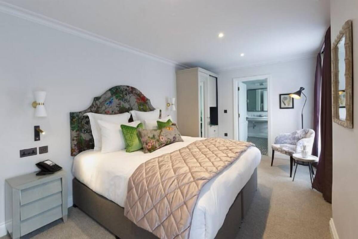A hotel room with a bed, bedside table, lamp, chair, wardrobe, and a mirror.
