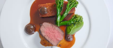 A plate with a slice of meat, broccoli, and two round objects, possibly sauces, on a white plate.