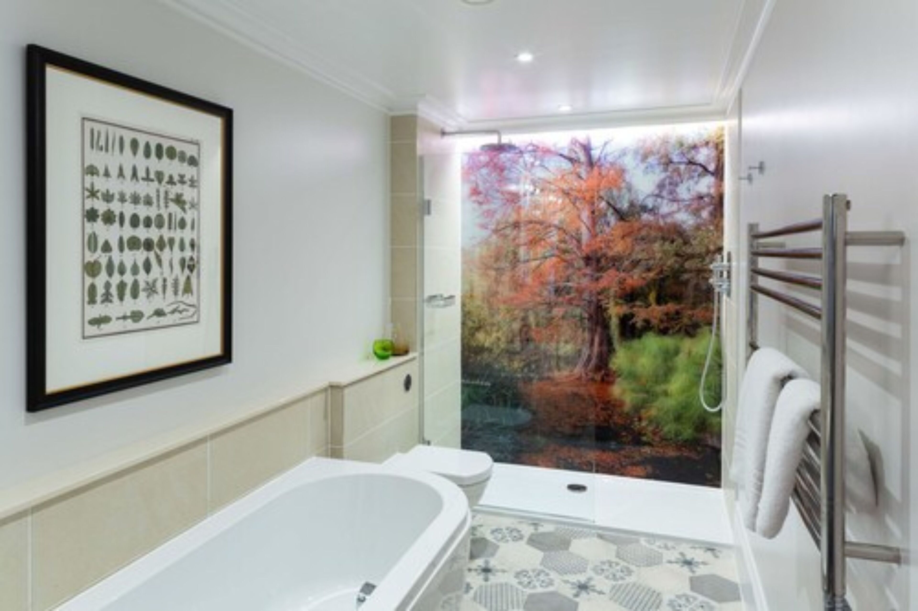 A modern bathroom with a bathtub, toilet, and a large window with a view of autumn trees.