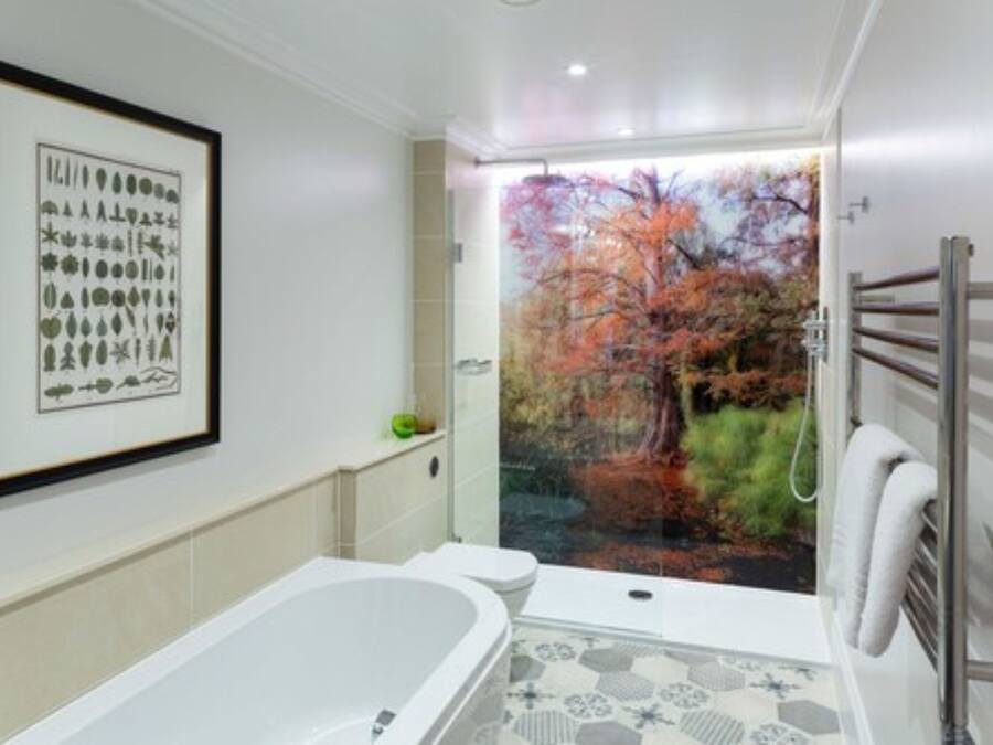 A modern bathroom with a bathtub, toilet, and a large window with a view of autumn trees.