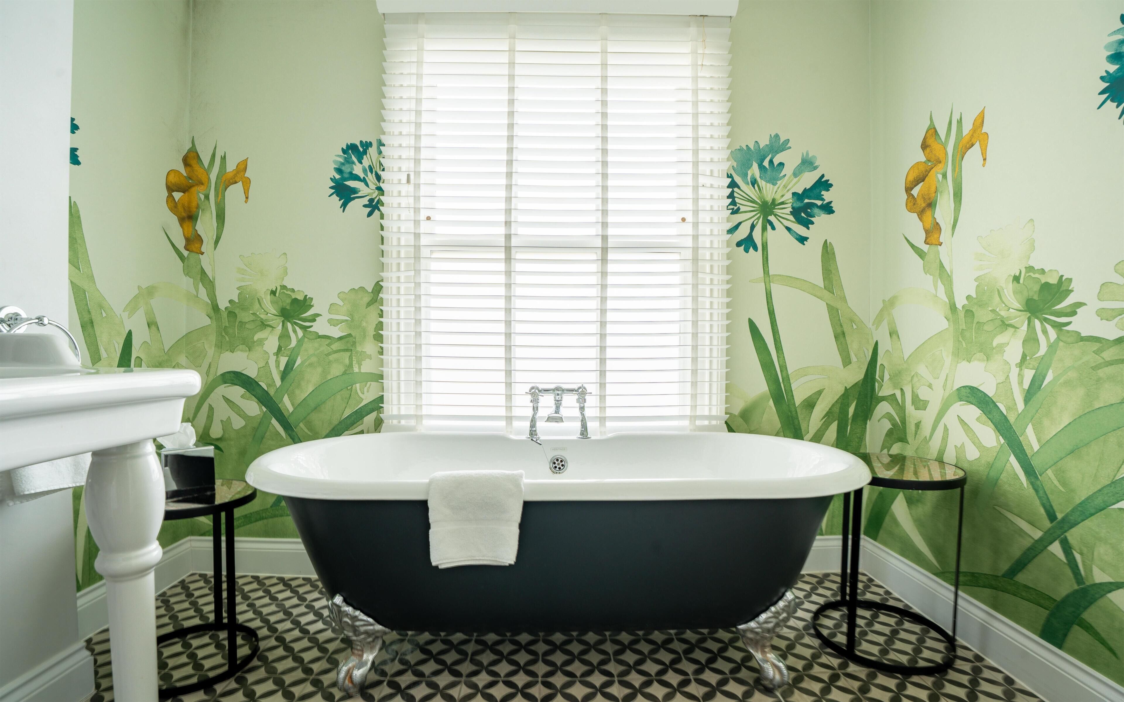 A bathroom with a freestanding bathtub, a sink, and a window with blinds.