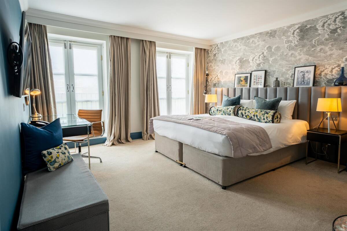 A hotel room with a large bed, a desk, a chair, and a view of the city.