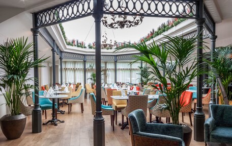 A spacious indoor dining area with multiple tables and chairs, a central decorative column, and potted plants.