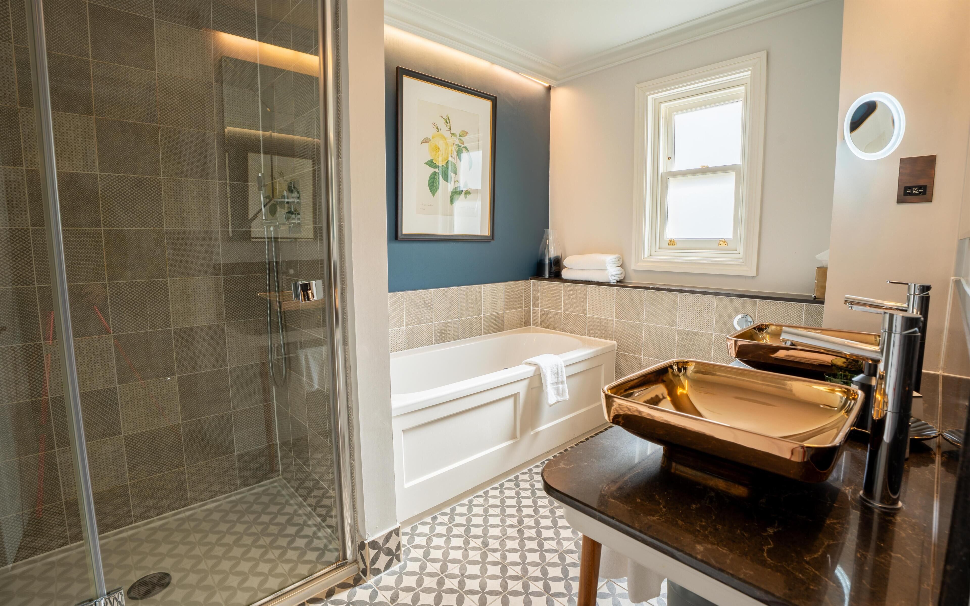 Un baño moderno con cabina de ducha de vidrio, bañera, tocador con espejo y ventana que proporciona luz natural.