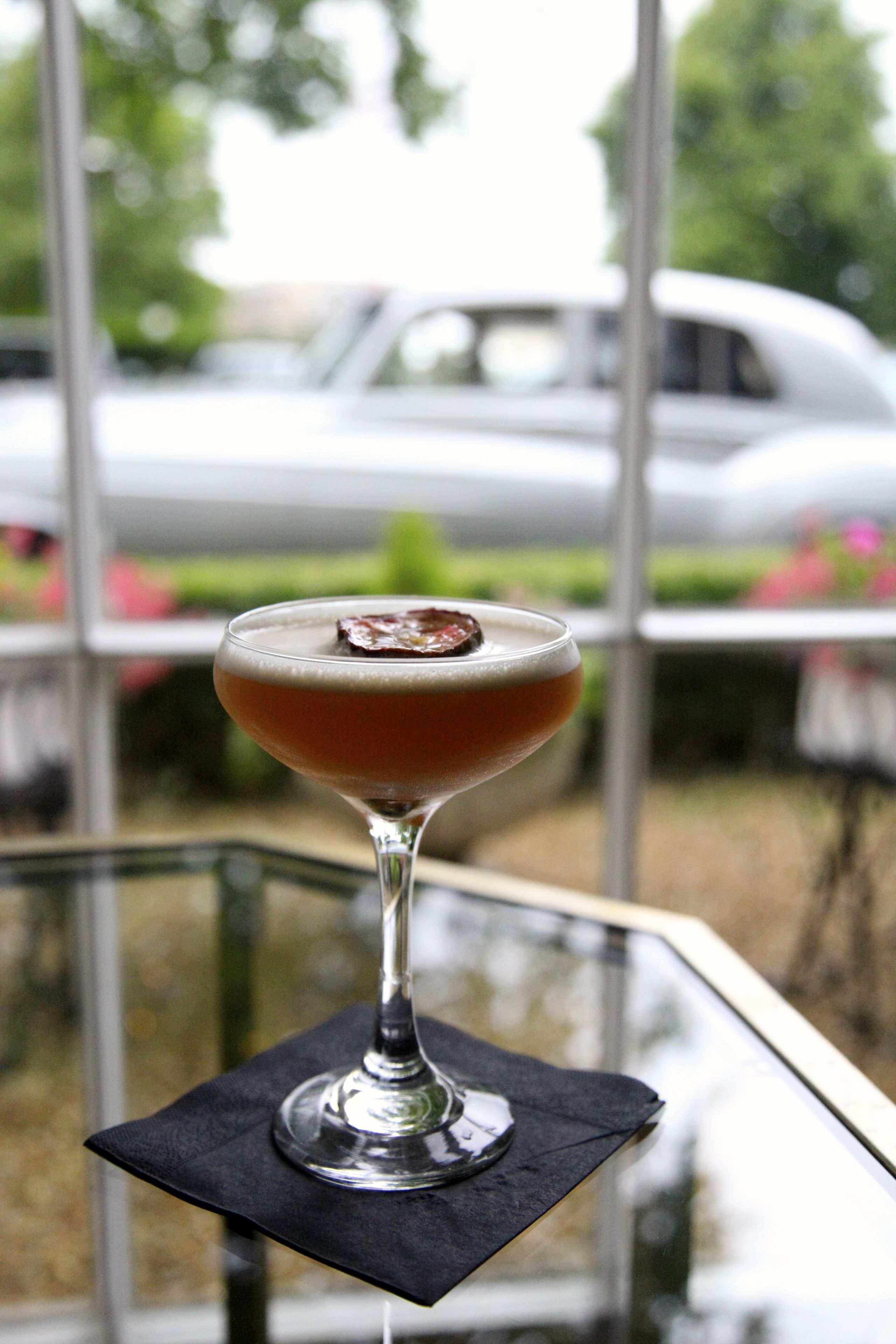 Un verre à cocktail, agrémenté d’une garniture, posé sur une serviette noire, lui-même placé sur une surface réfléchissante.
