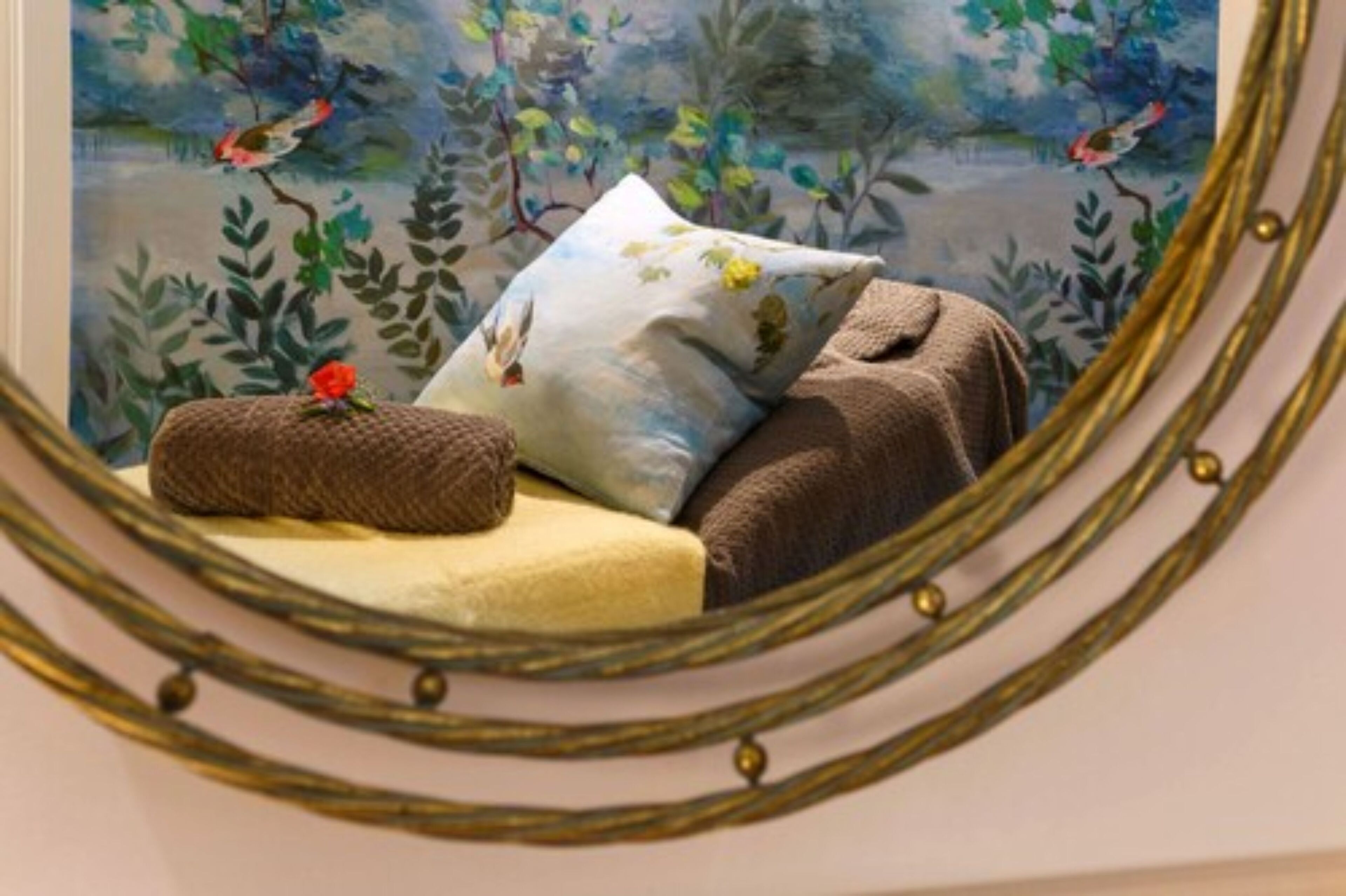Una cama con un cojín floral, una manta marrón y un pequeño cojín con una flor roja.