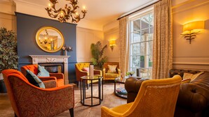 A well-lit living room with a fireplace, multiple seating options, and large windows with curtains. - The Gonville Hotel, a member of Radisson Individuals (Cambridge)