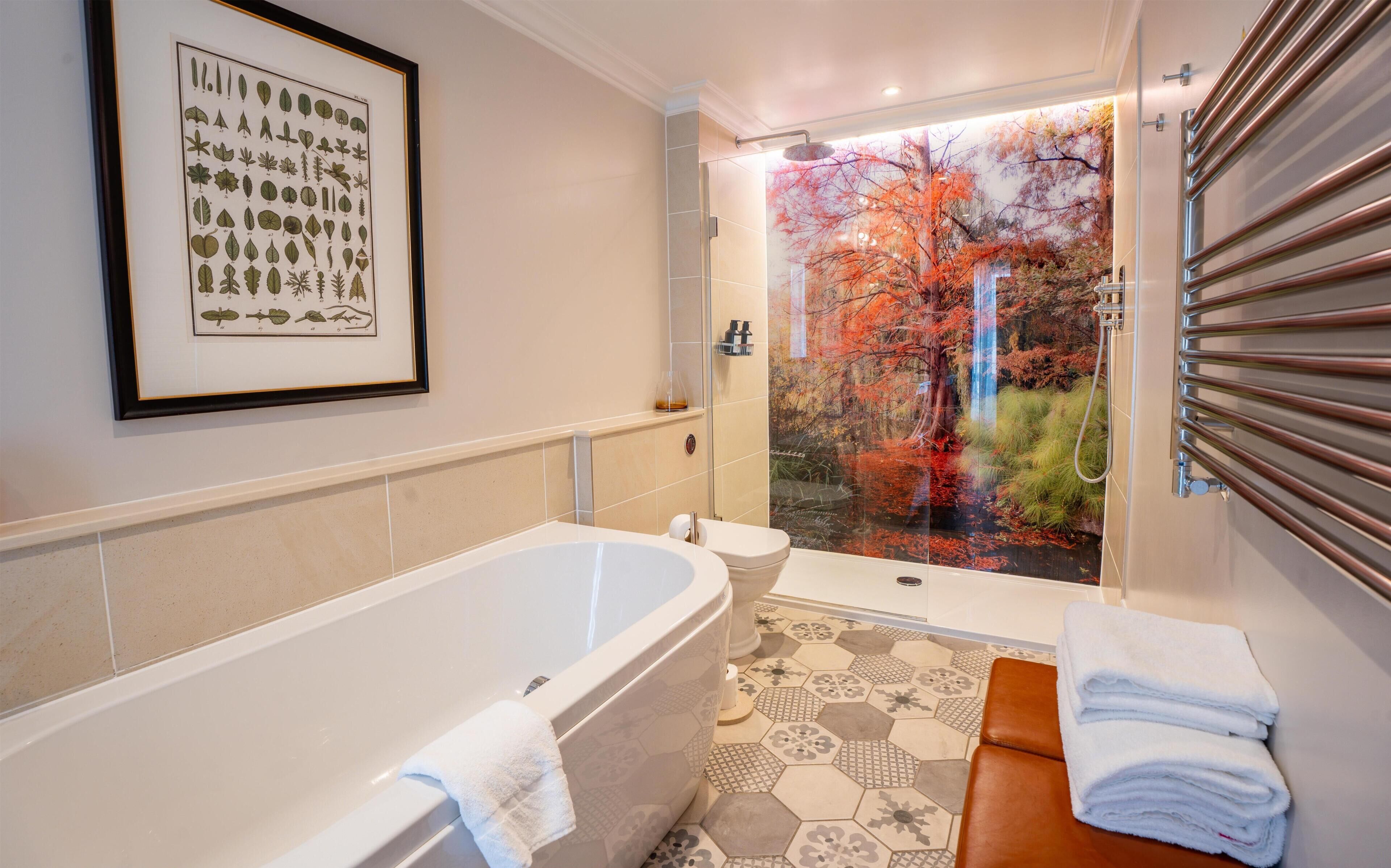 Une salle de bain avec une baignoire, des toilettes et une douche donnant sur les arbres aux couleurs automnales.