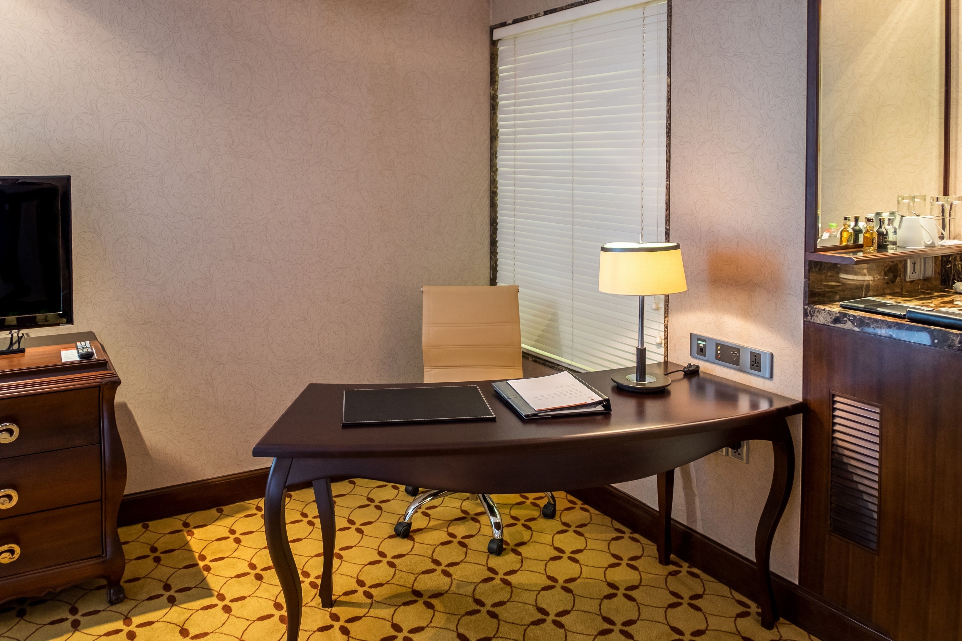 Una habitación de hotel con escritorio, lámpara, televisor y minibar.