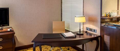 Una habitación de hotel con escritorio, lámpara, televisor y minibar.