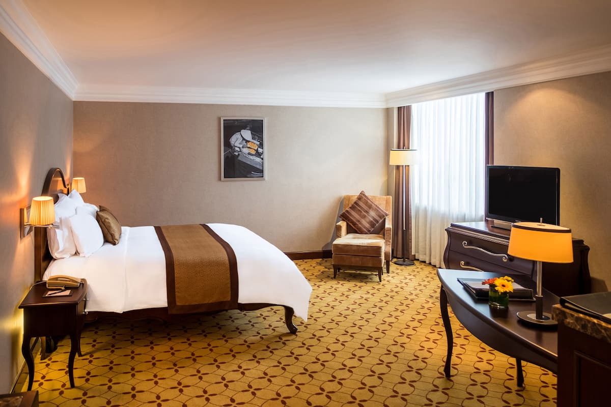 Una habitación de hotel con cama, escritorio, silla, televisor y lámpara.