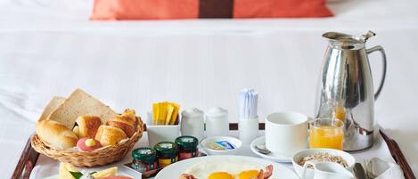 A breakfast tray with toast, eggs, bacon, and fruit on a hotel bed.
