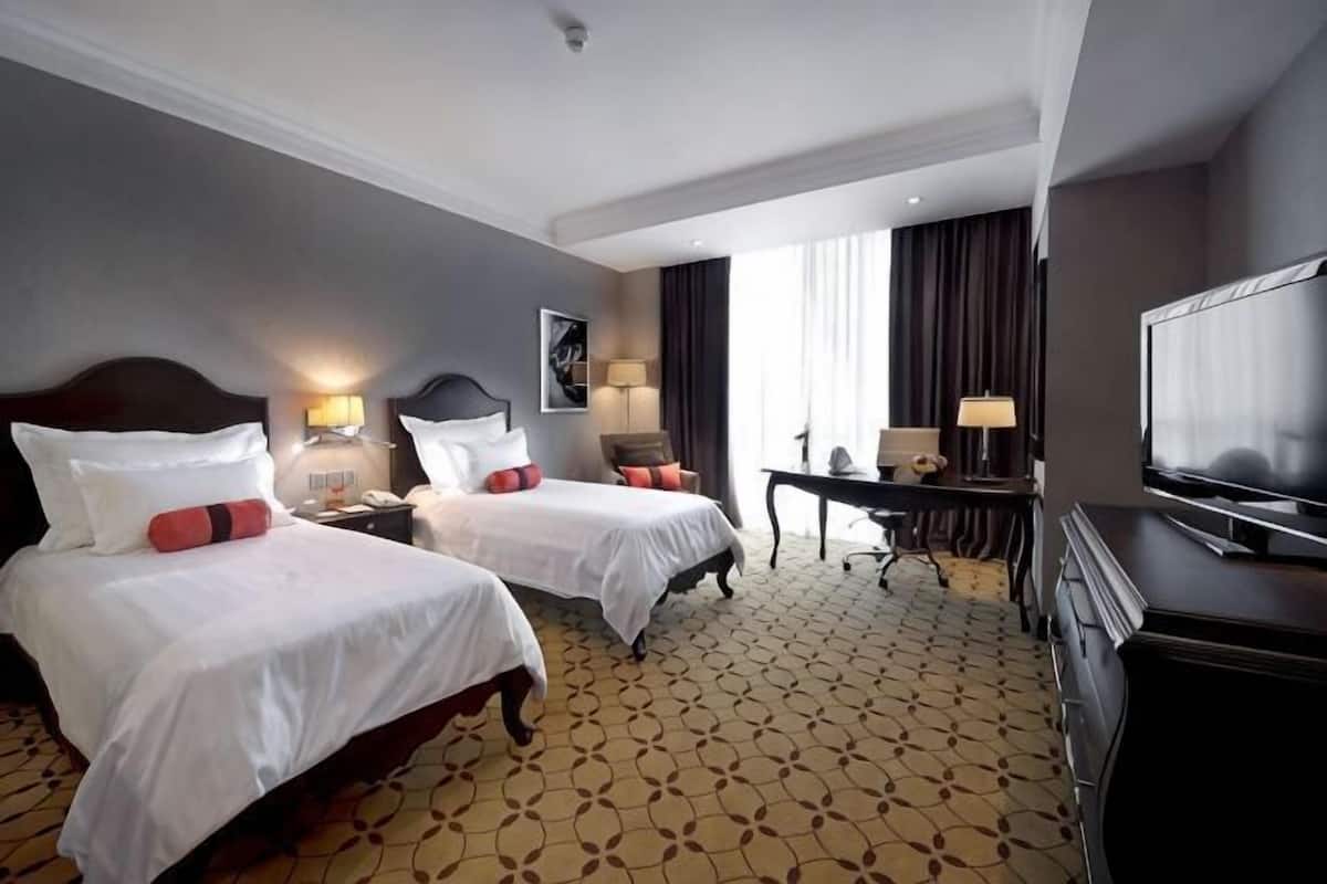 Habitación de hotel con dos camas, un escritorio, una silla, televisión y ventana con cortinas.