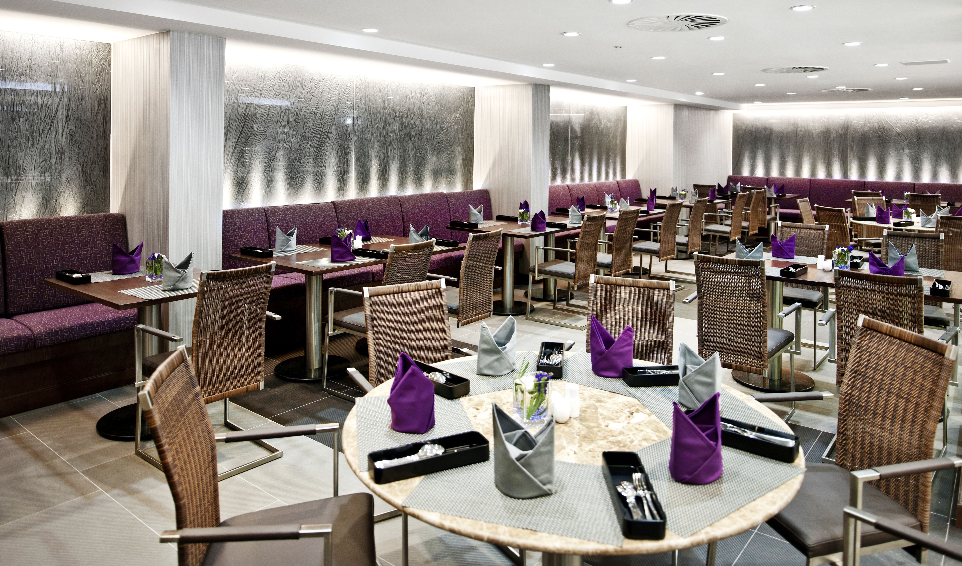 A modern restaurant with purple seating, round tables, and wicker chairs.