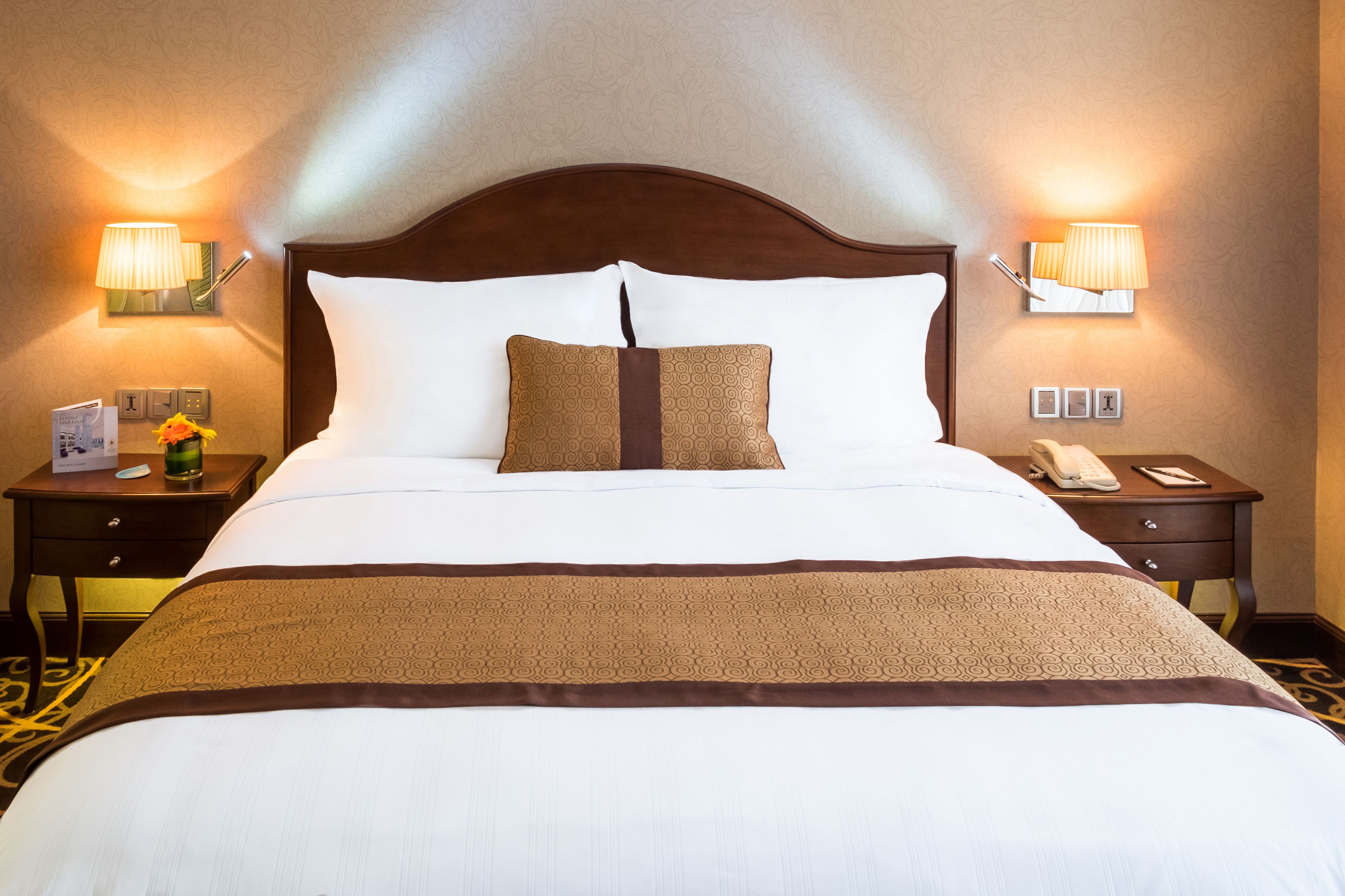 Una habitación de hotel con una cama grande, dos mesitas de noche, una lámpara y un teléfono.