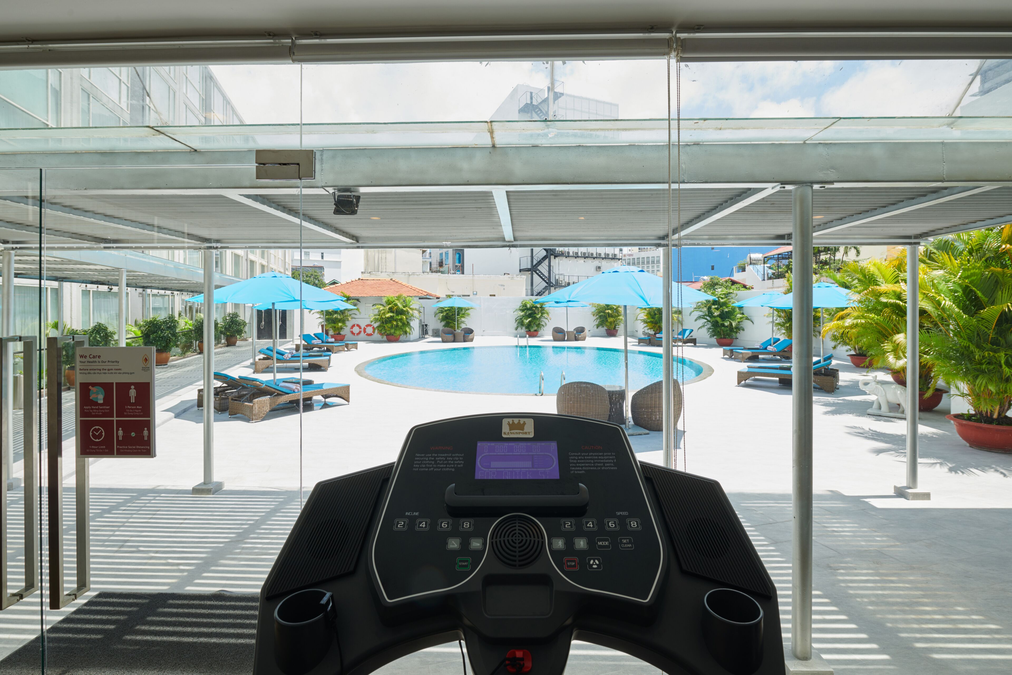 A gym area with a treadmill, a pool, and outdoor seating with umbrellas.