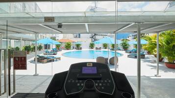 A gym area with a treadmill, a pool, and outdoor seating with umbrellas.