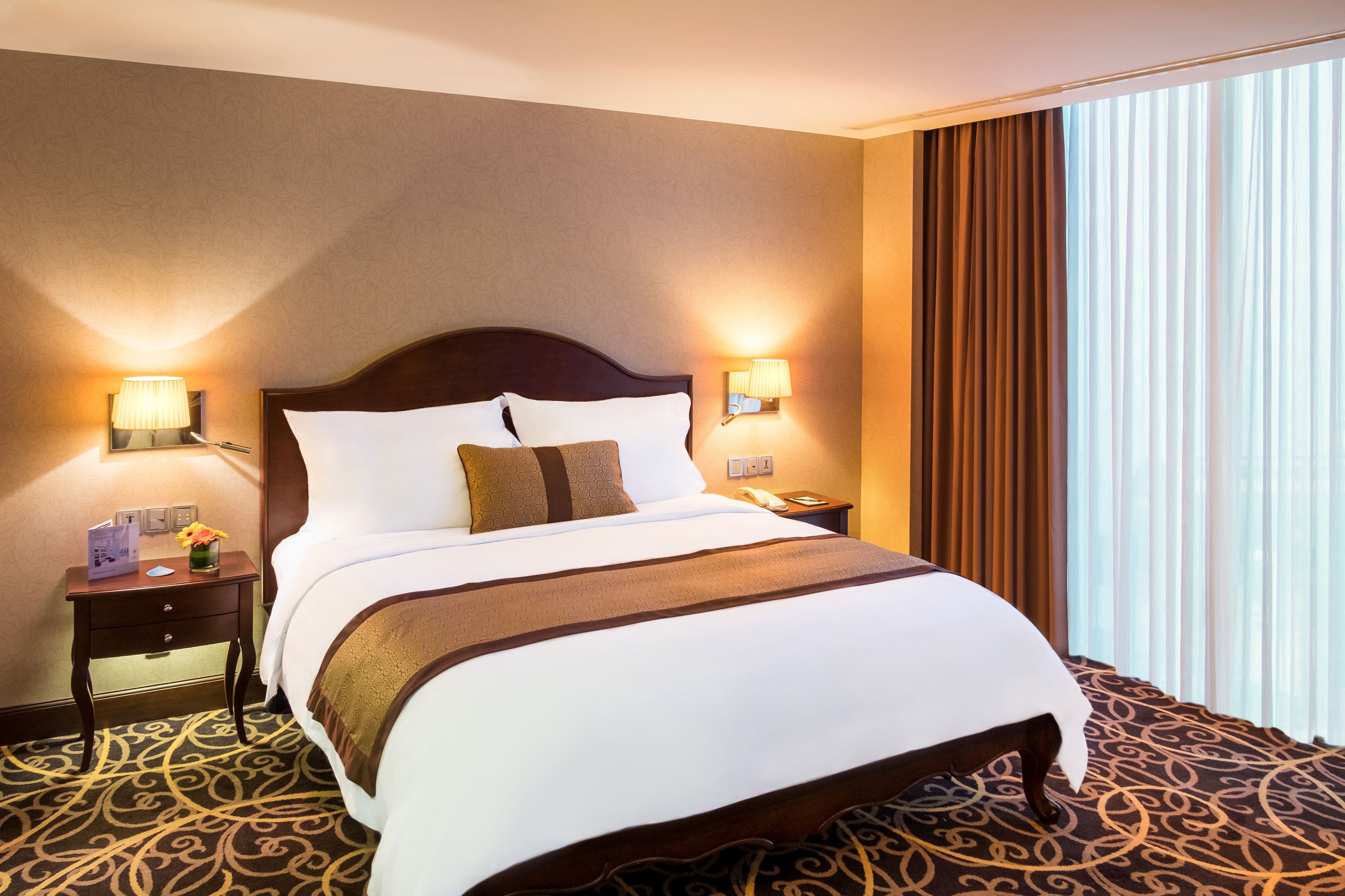 Una habitación de hotel con una cama grande, dos mesitas de noche, un teléfono y una ventana con cortinas.