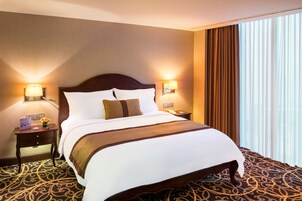 A hotel room with a large bed, two bedside tables, a nightstand, a telephone, and a window with curtains.