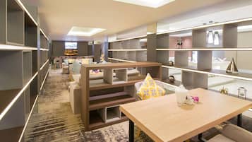 A modern hotel room with a large bed, a desk, and a TV. There are shelves with decorative items and a carpeted floor.