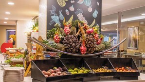 Un bufé con diversas frutas y verduras, una pizarra con dibujos de frutas y una pila de platos.
