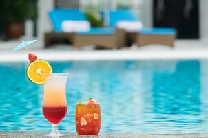 Two cocktails by a poolside with lounge chairs in the background.