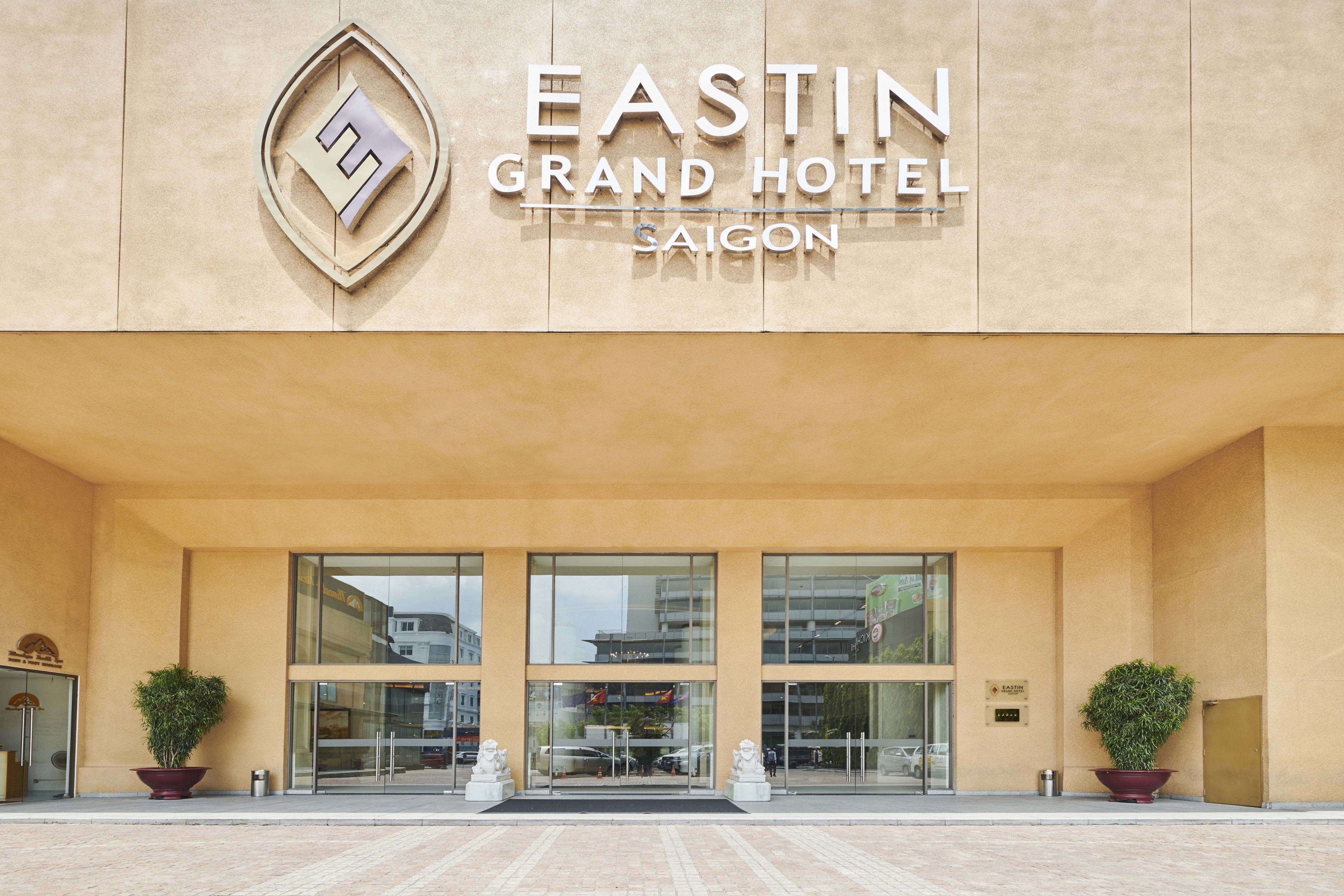 The EASTIN GRAND HOTEL SAIGON facade with a modern design, large glass entrance, and two potted plants on either side.