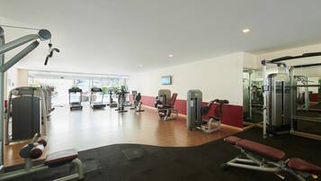 A gym with various exercise machines, a bench, and a mirrored wall.