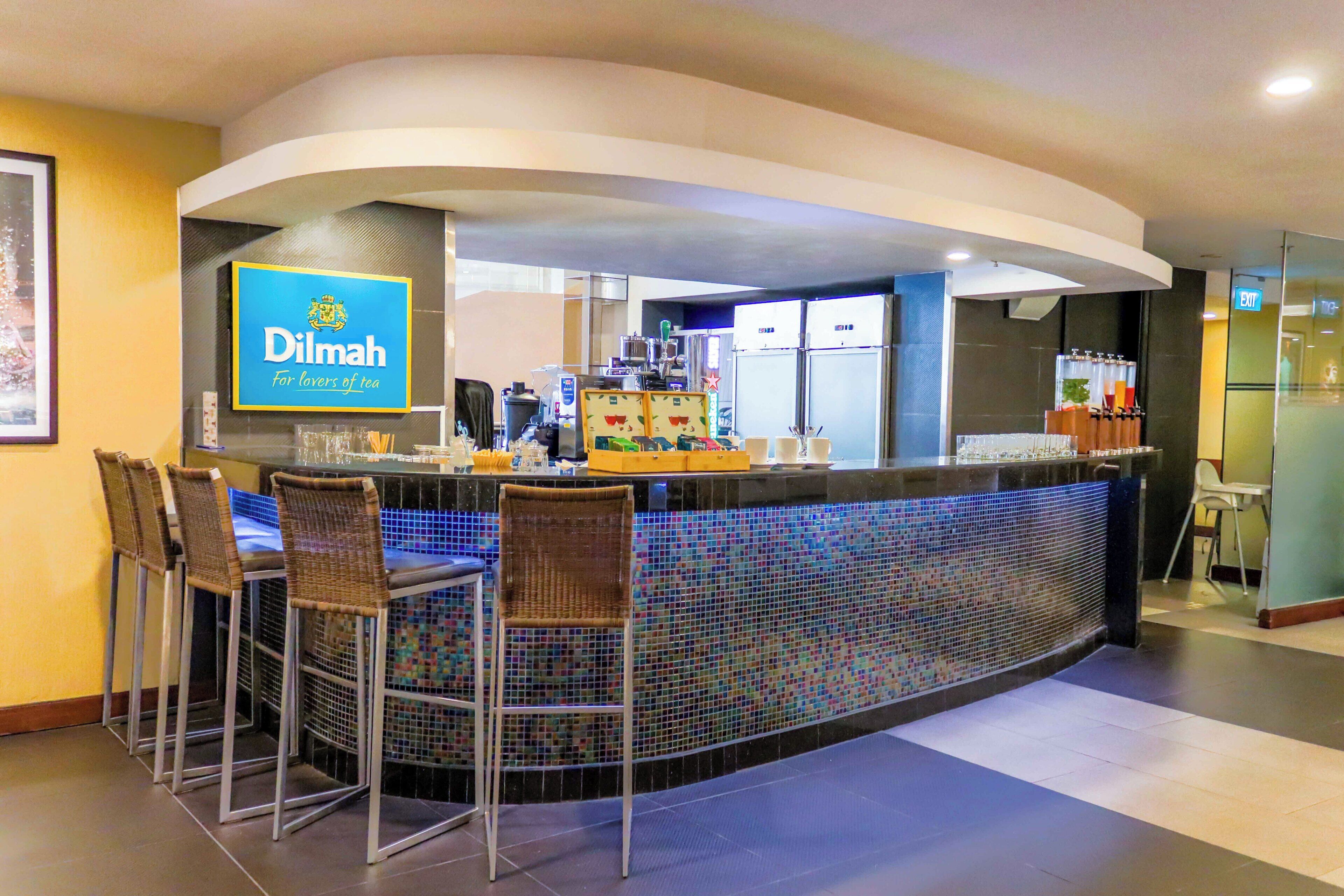 Zona de bar moderna con barra, taburetes y un cartel que dice 'Dilmah Para los amantes del té'.