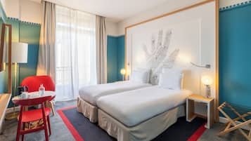 Et hotelværelse med to senge, en rød lænestol, et lille bord med en lampe og et stort abstrakt maleri på væggen.