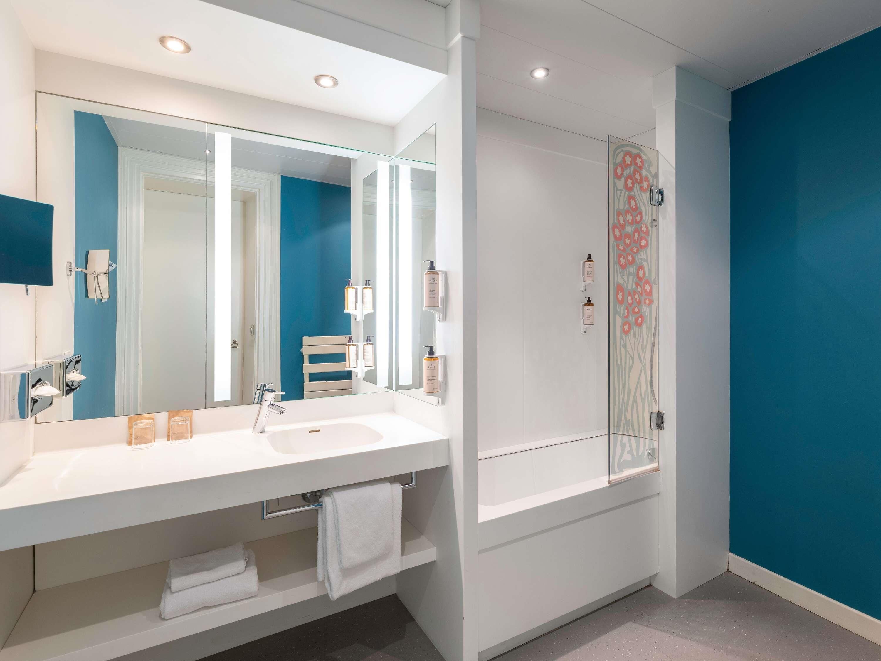 A modern bathroom with a large mirror, white sink, and a glass shower enclosure.