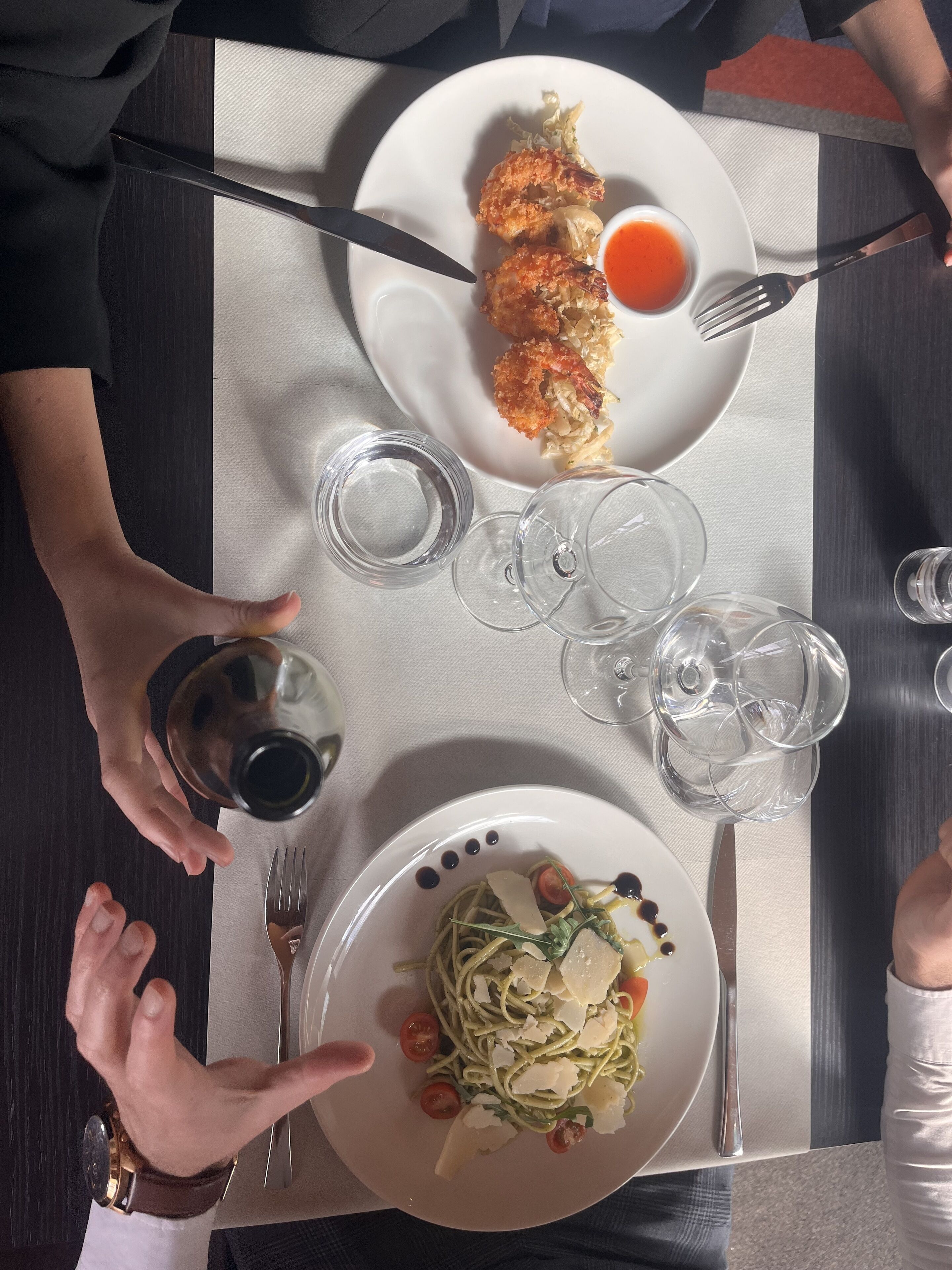 A dining table with plates of food, wine glasses, and cutlery.