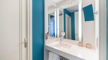 Un baño con un lavabo blanco, un espejo grande y una pared azul decorativa.