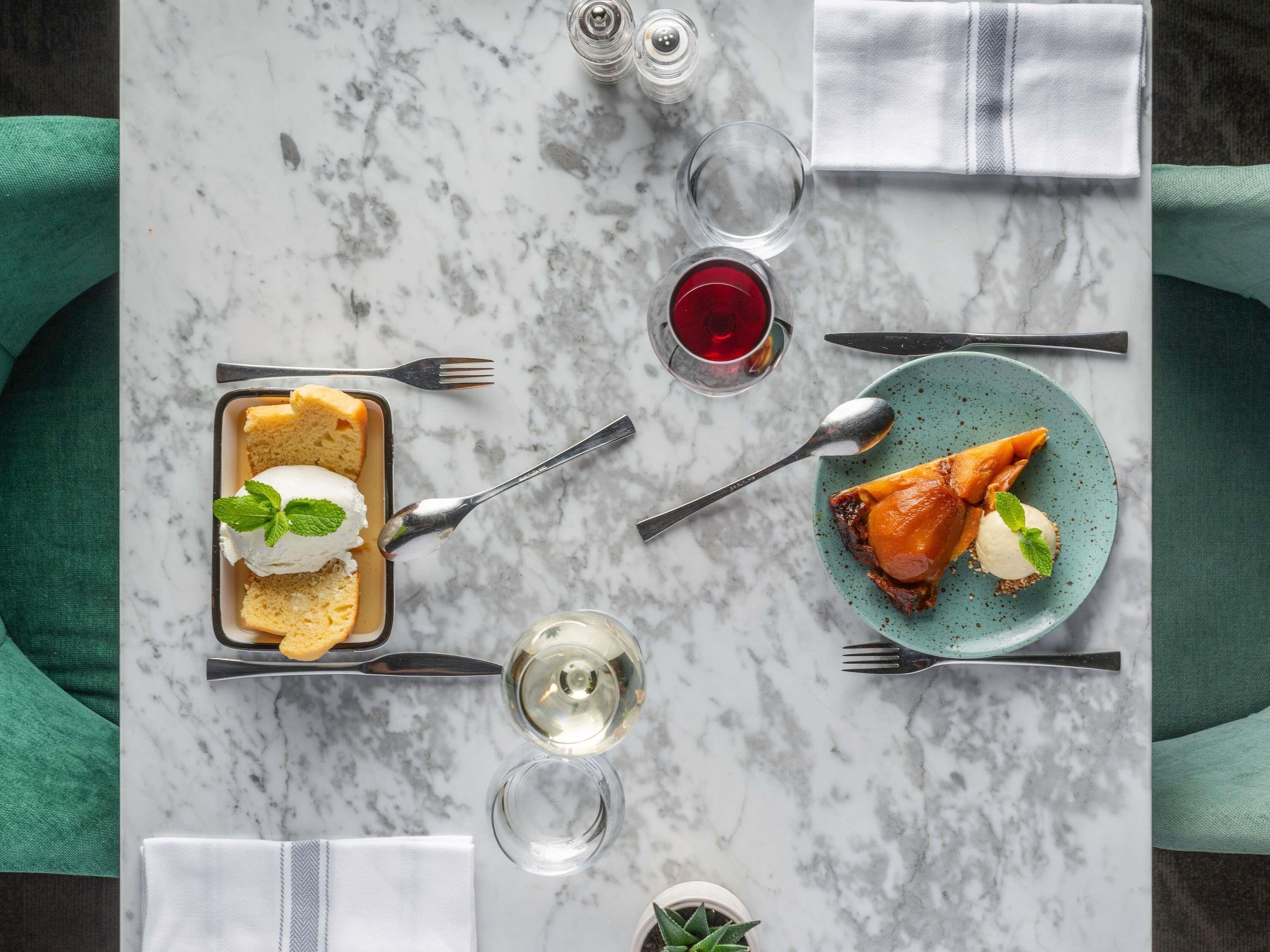 A marble table with a dessert tray, plates with food, wine glasses, and cutlery.