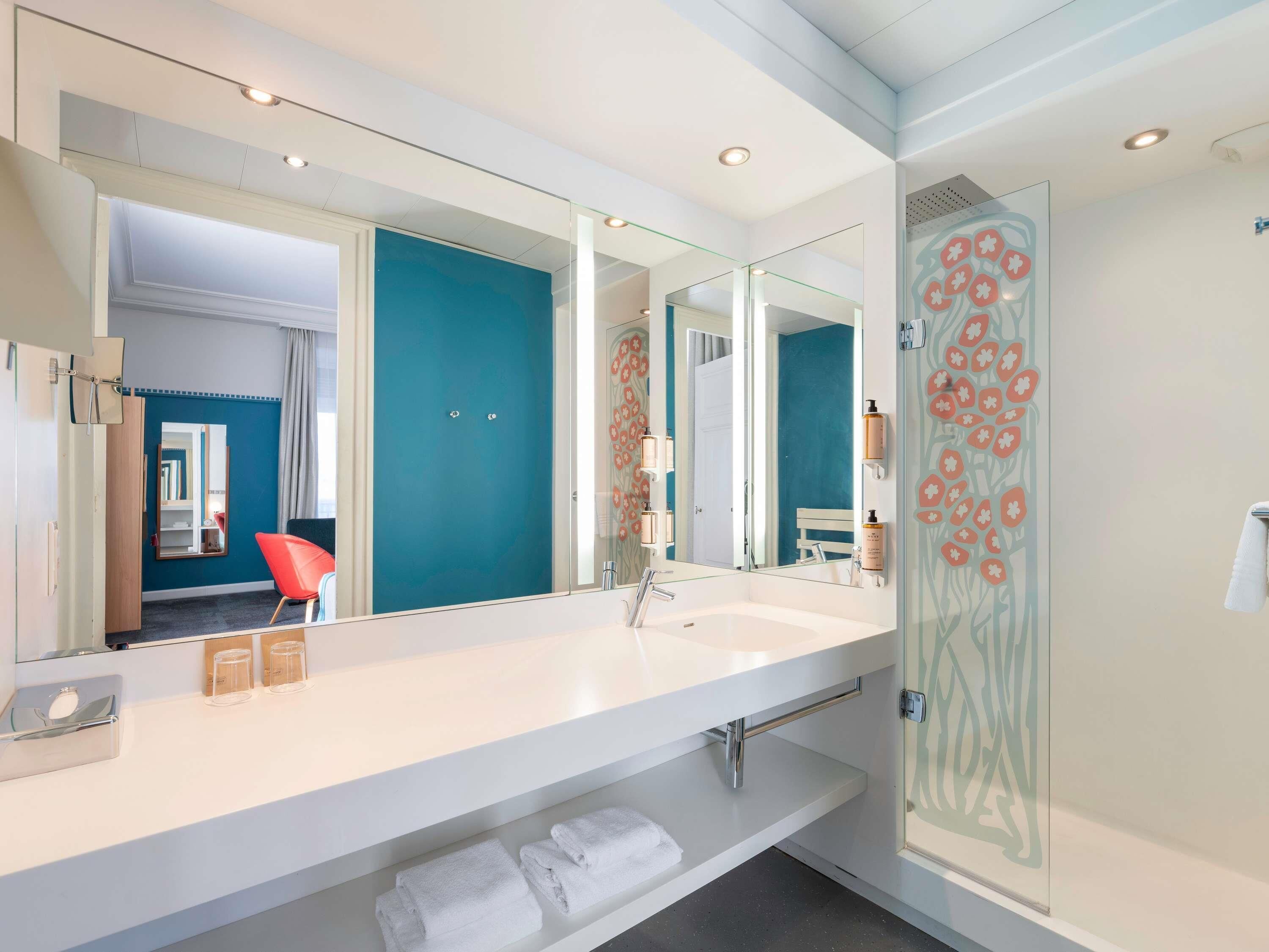 Une salle de bain moderne avec un grand miroir, un lavabo blanc et une cabine de douche en verre.
