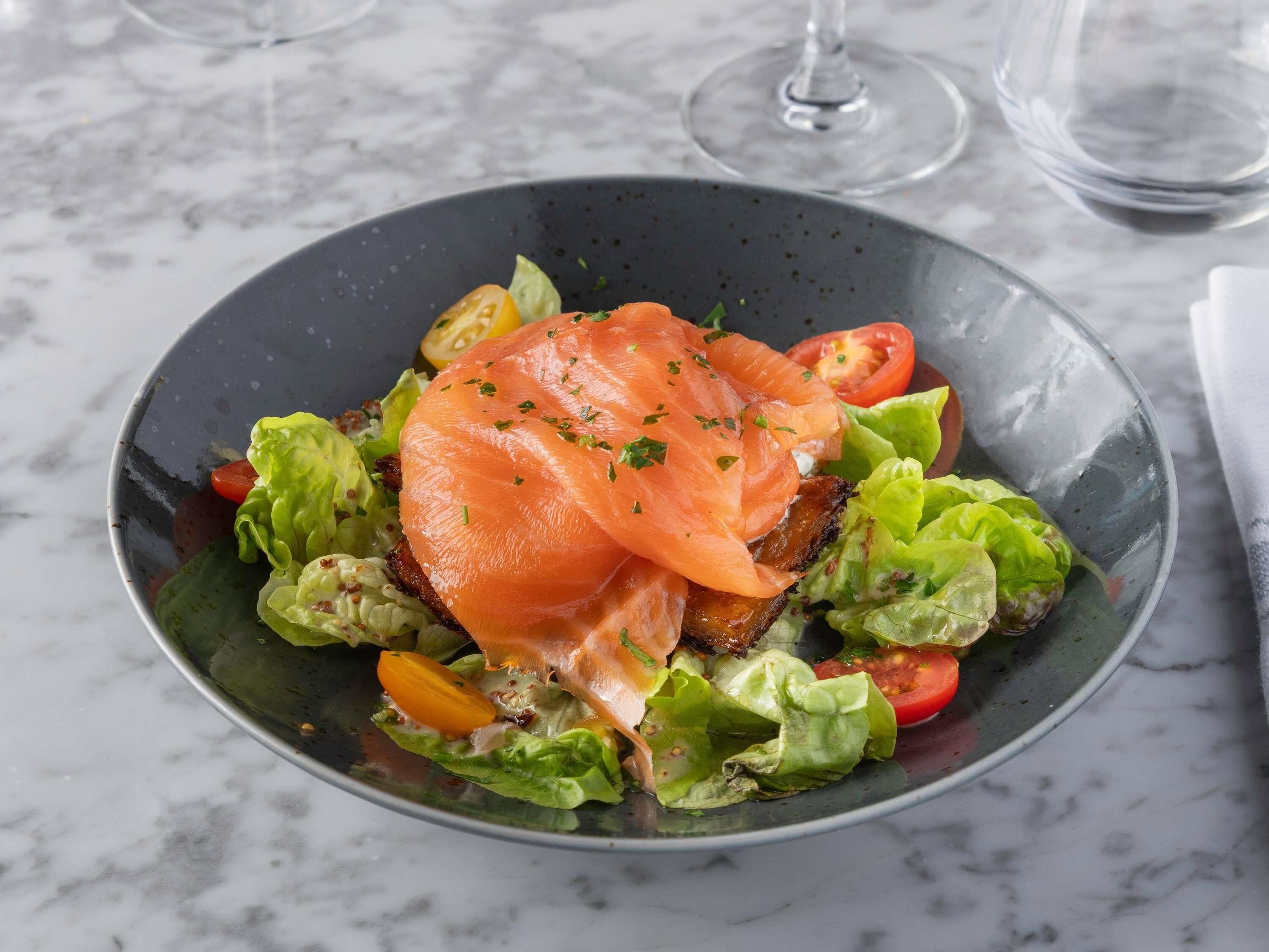 Un tazón de comida con salmón, lechuga y tomates.