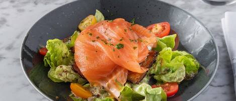 Un tazón de comida con salmón, lechuga y tomates.