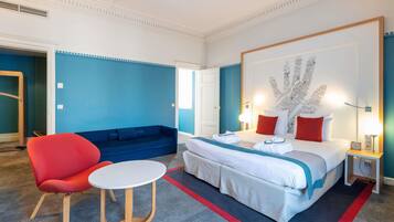 A hotel room with a bed, a red chair, a round table, and a blue sofa.