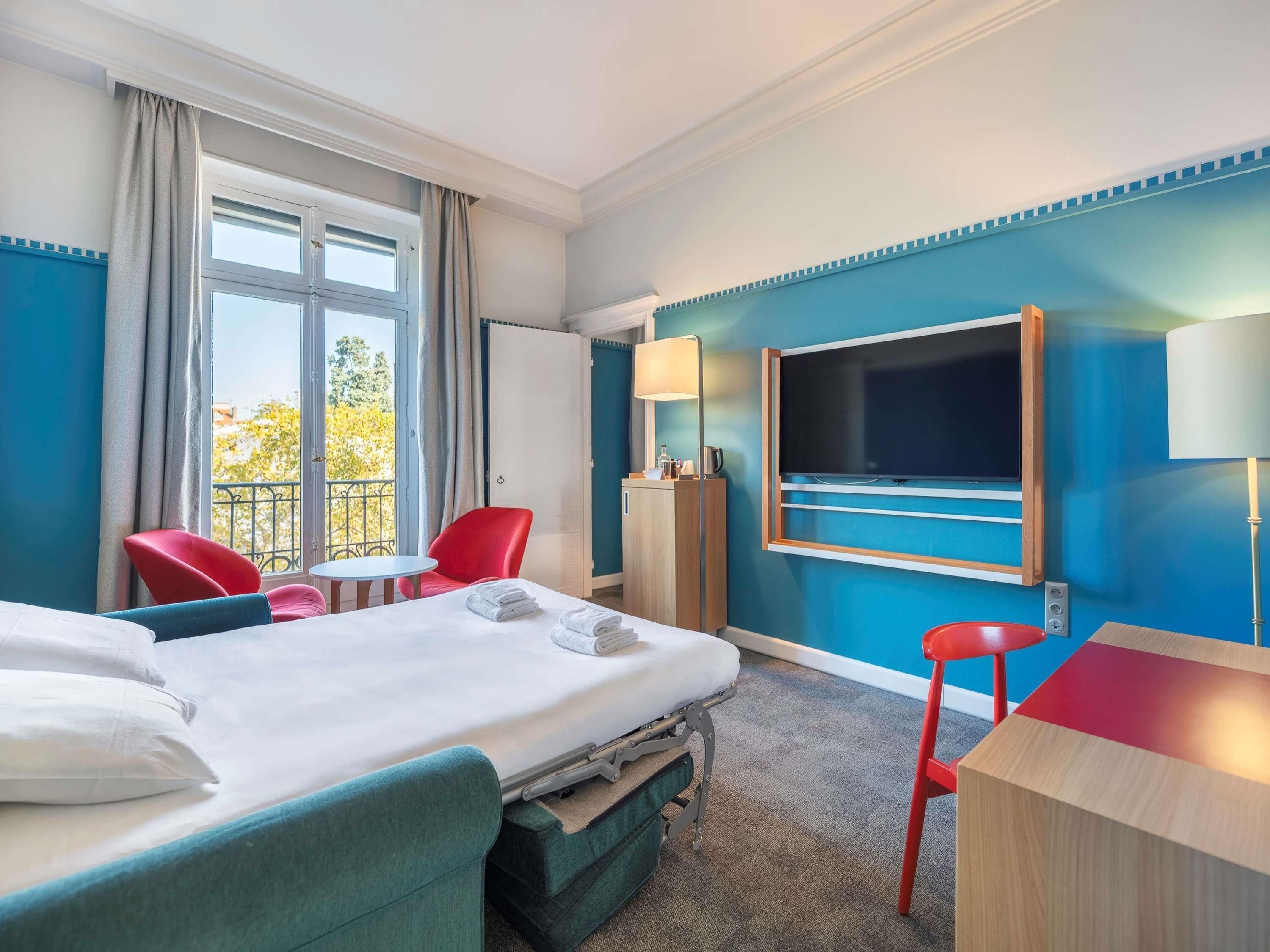 Ett hotellrum med en säng, ett skrivbord, en tv, en stol och utsikt över omgivningarna.