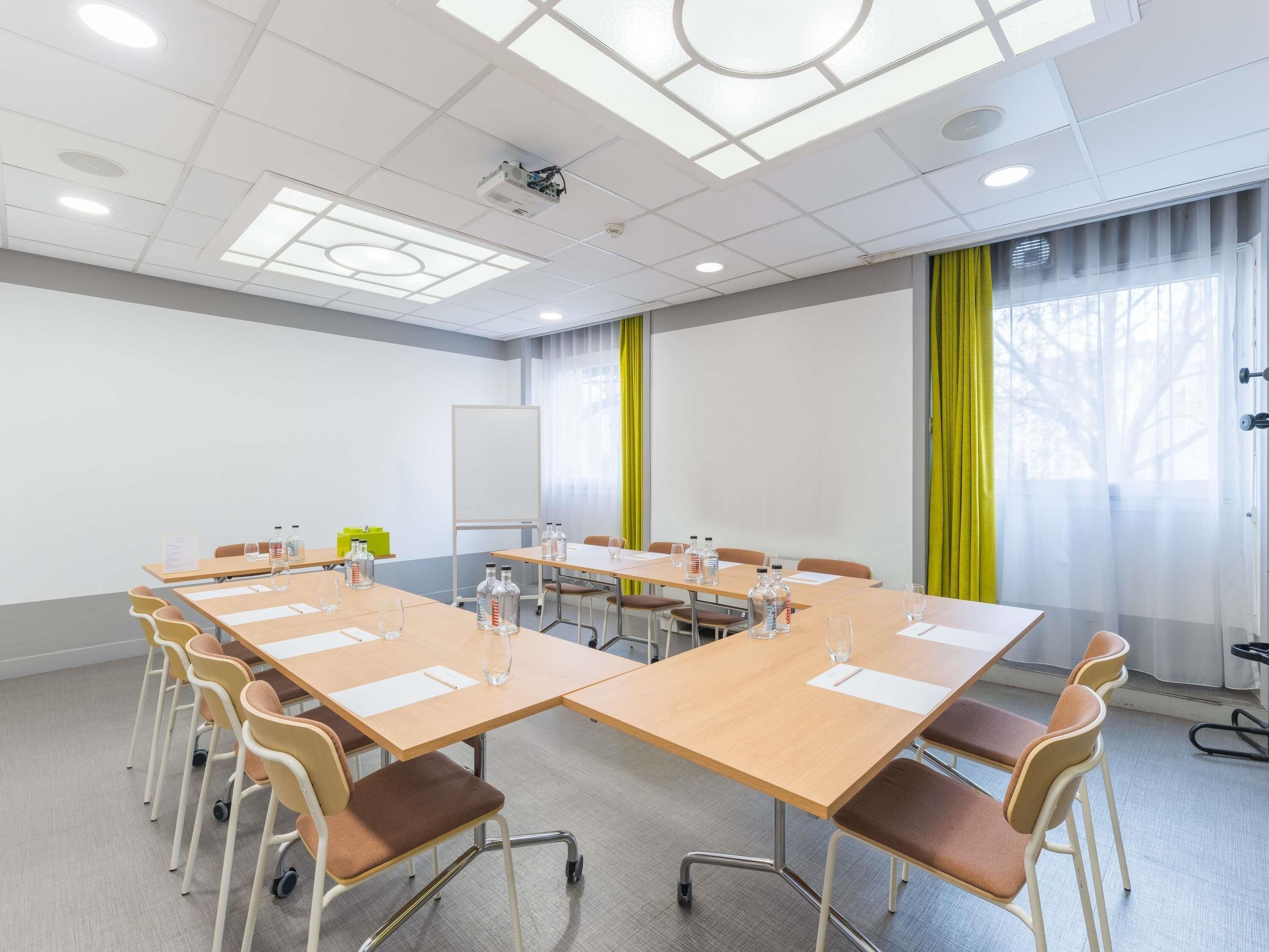 Un salón de conferencias con una gran mesa, sillas, un proyector, una pizarra y un ventanal con cortinas.