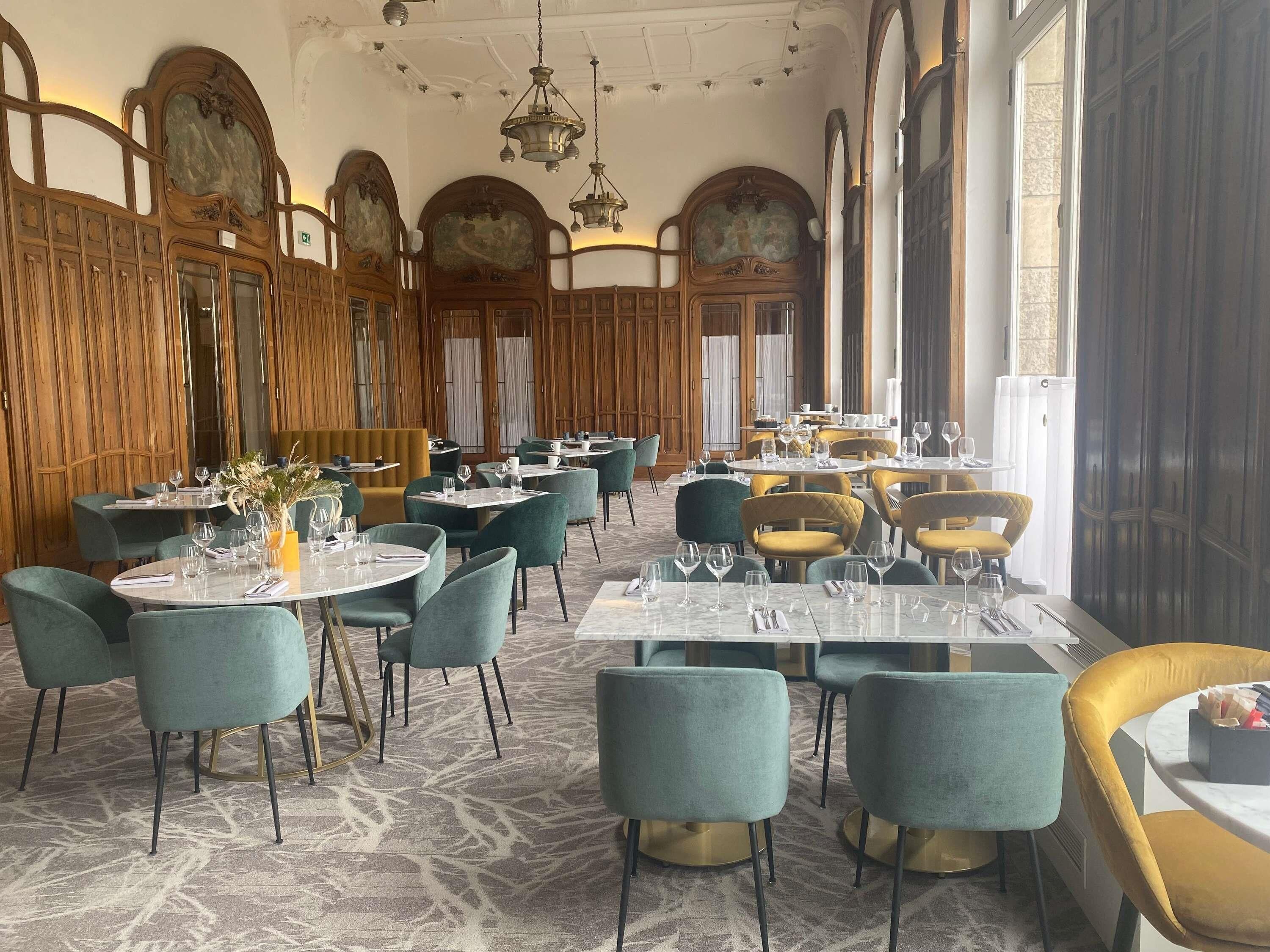 Een restaurant met ronde tafels, groene en gele stoelen en een marmeren vloer.