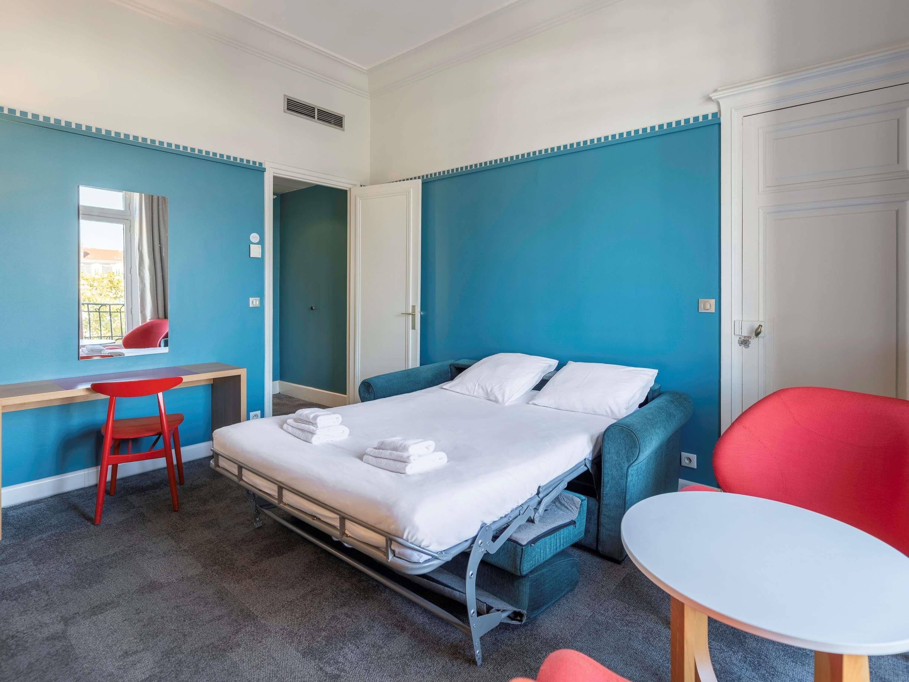 Une chambre d’hôtel de taille réduite, comprenant un lit, un bureau, une chaise et une petite table.
