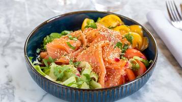 A bowl of food with salmon, vegetables, and sesame seeds.