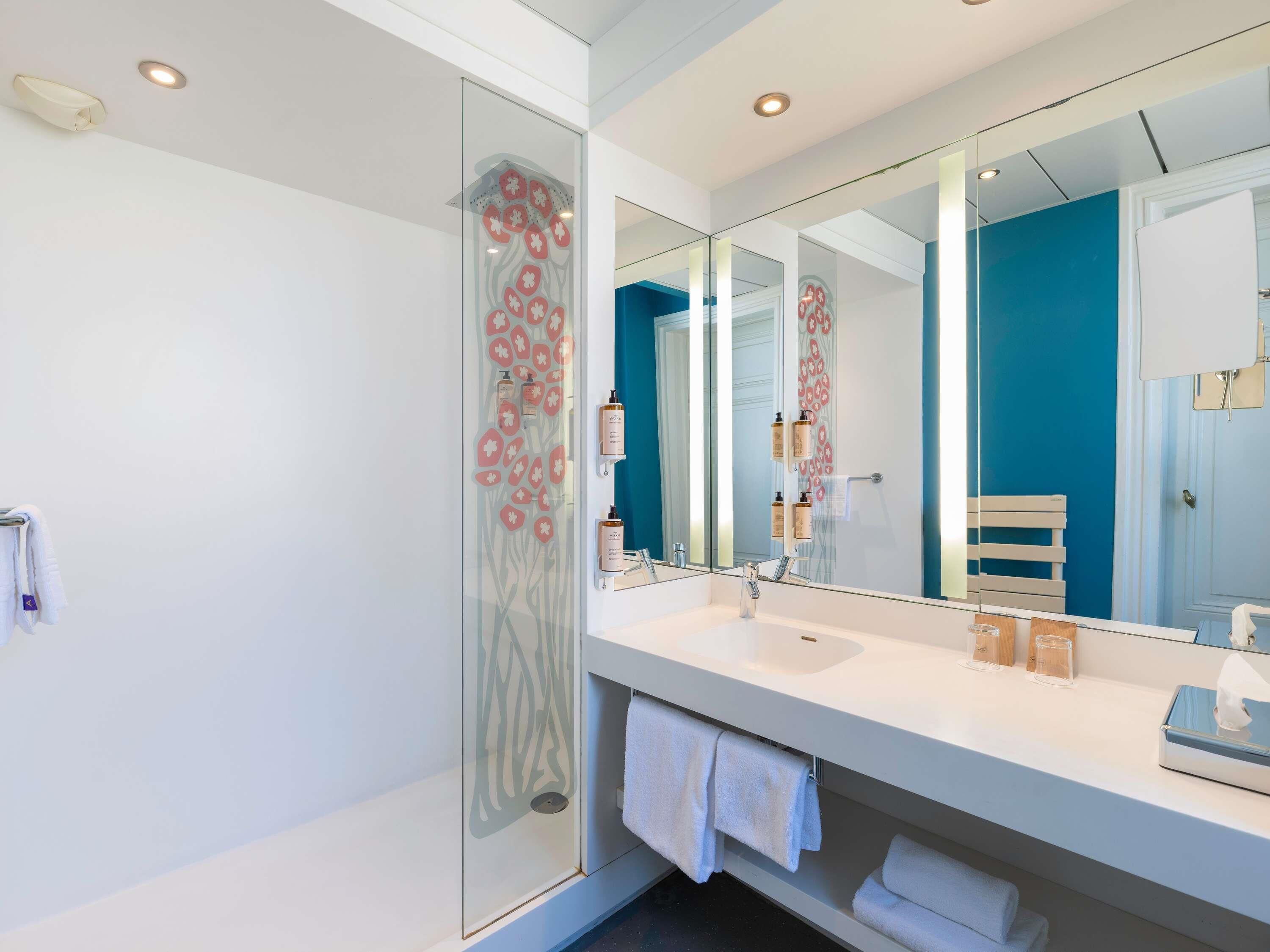 A modern bathroom with a glass shower enclosure, a large mirror, and a white vanity with a sink.
