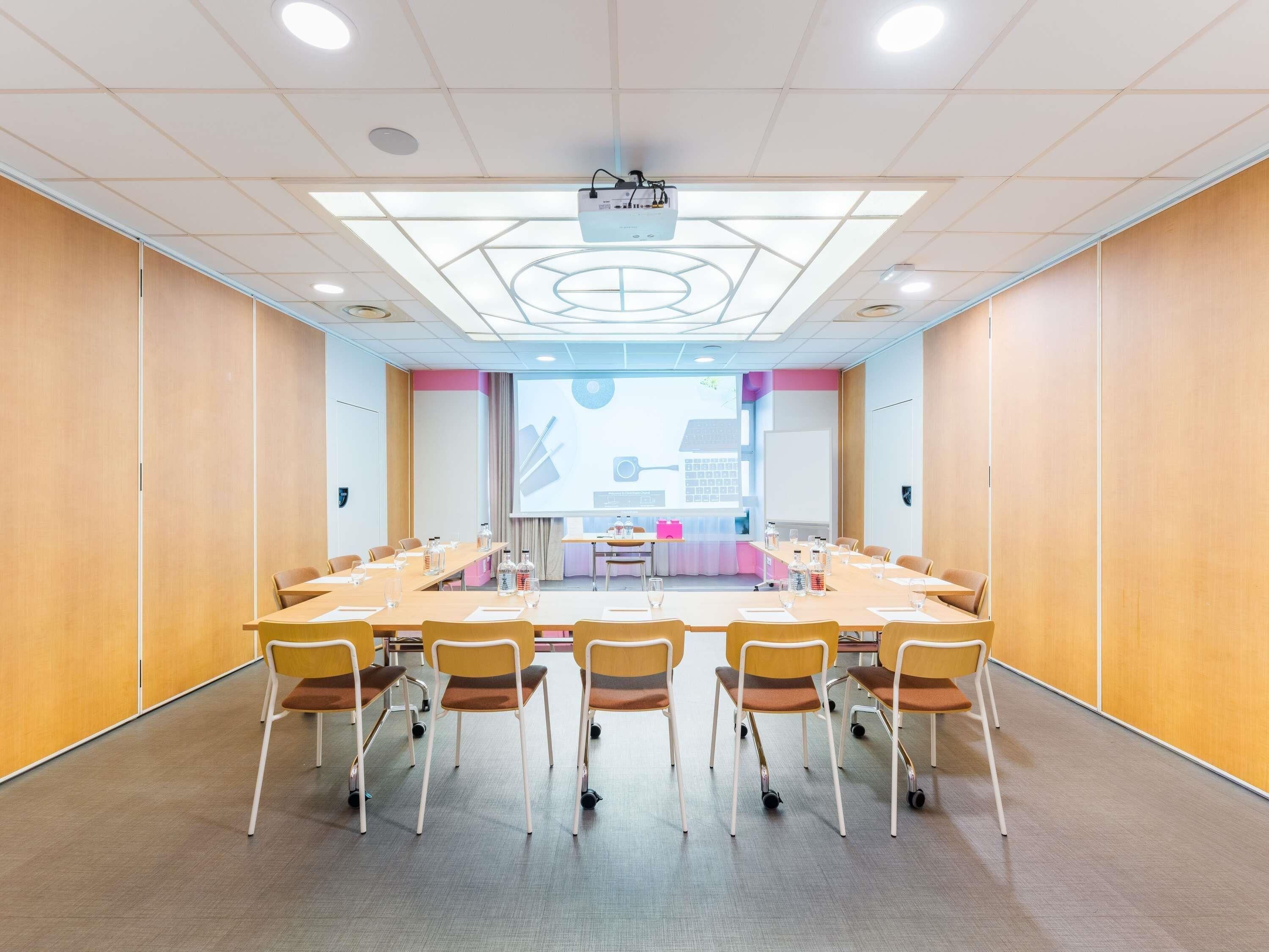 Een vergaderzaal met een lange tafel, stoelen, een beamer en een presentatiescherm.