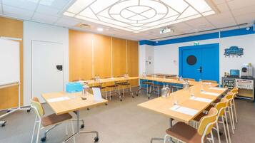Une salle de conférence équipée de tables, de chaises, d’un projecteur et d’une porte bleue.