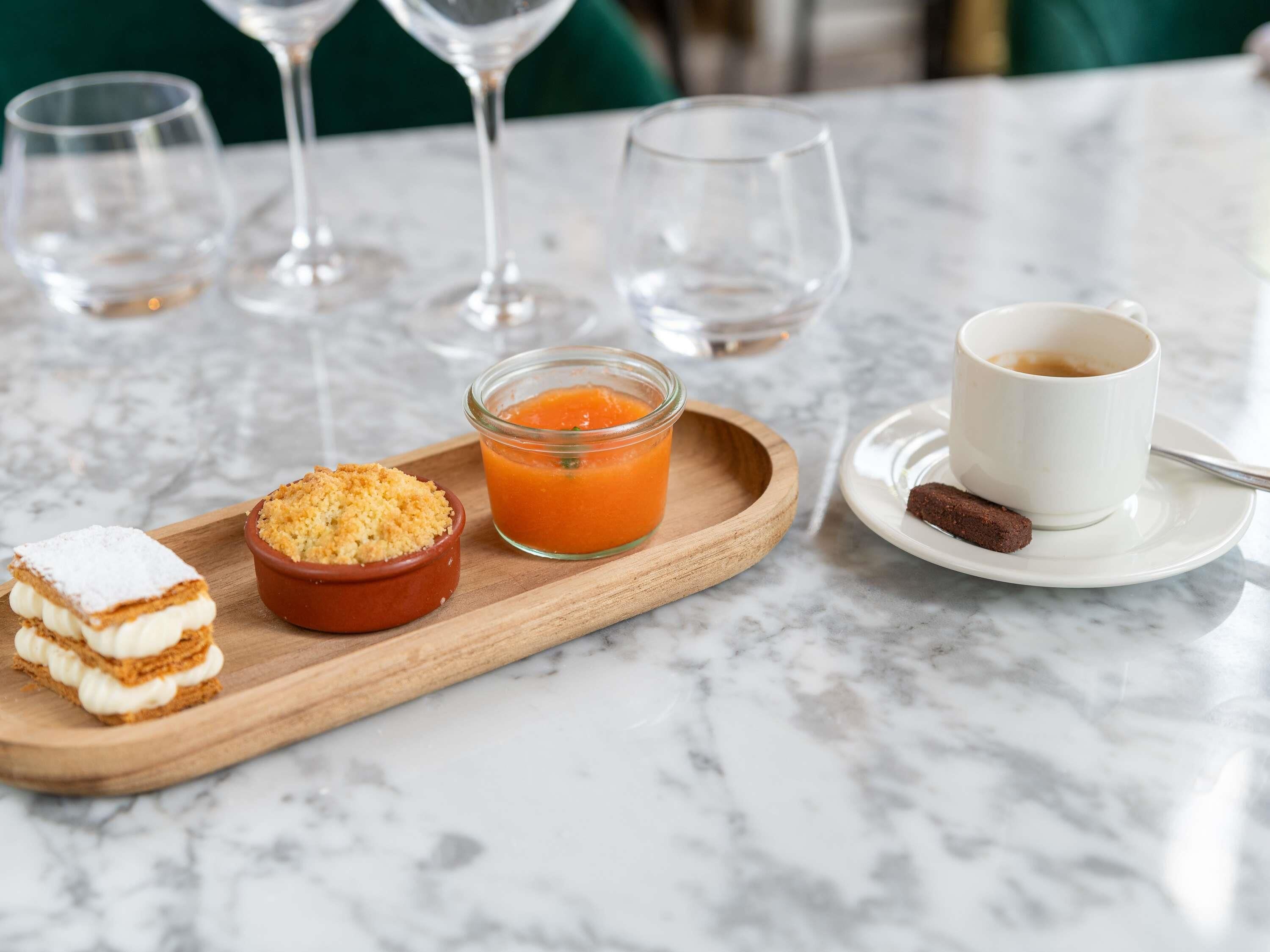 Una bandeja con pastel en capas, un cuenco de compota de frutas y una taza de café sobre una mesa de mármol.