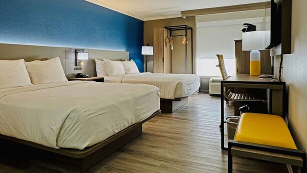 Een hotelkamer met twee bedden, een bureau met stoel, een televisie en een raam.