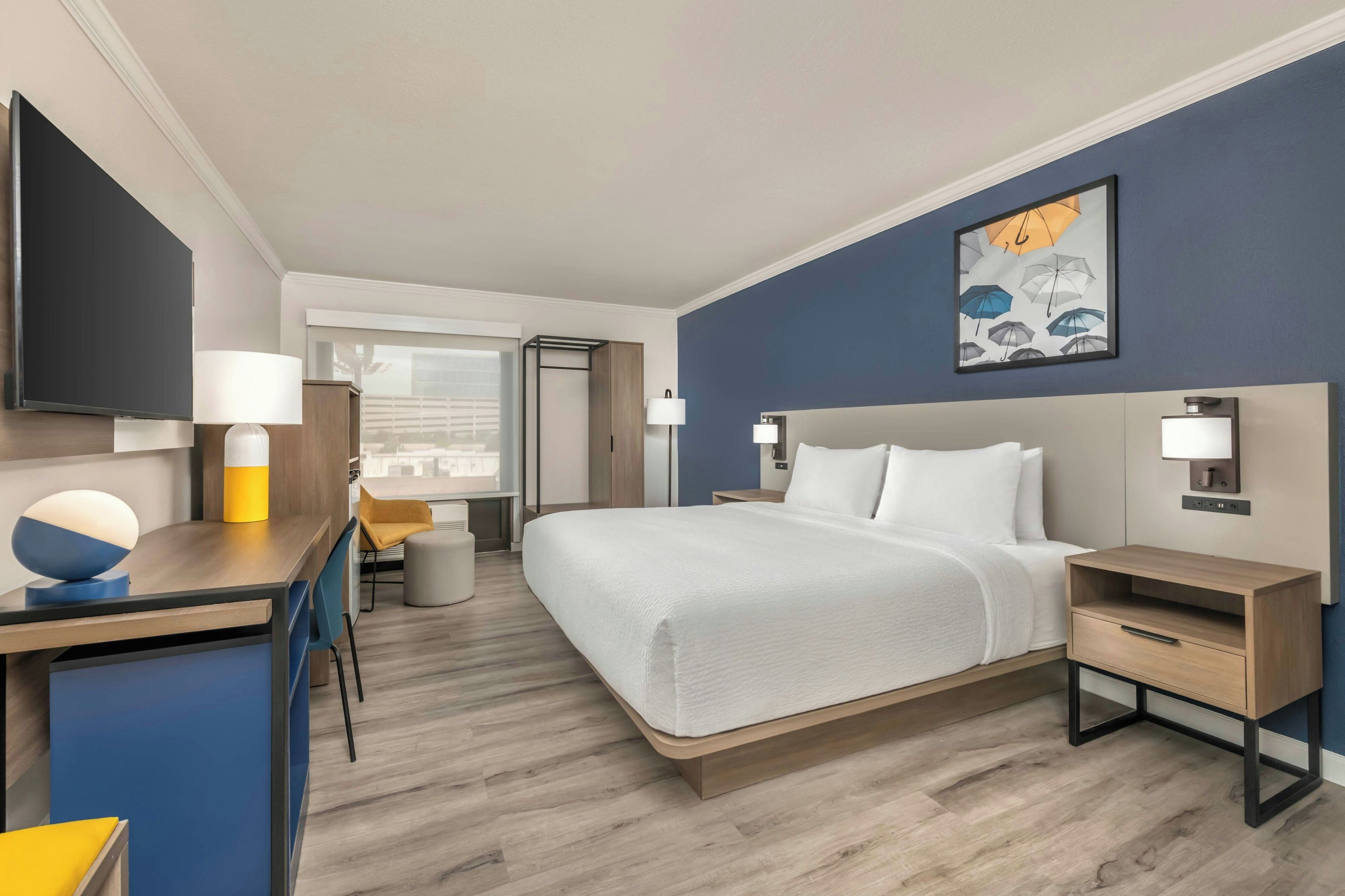 A hotel room with a bed, bedside tables, a desk with a chair, a TV, and a window with a view.
