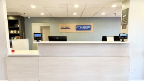 A reception desk with a 'Welcome City Express by Marriott' sign, two computer monitors, and a security camera on the ceiling. - City Express by Marriott I-10 West Energy Corridor (Houston)